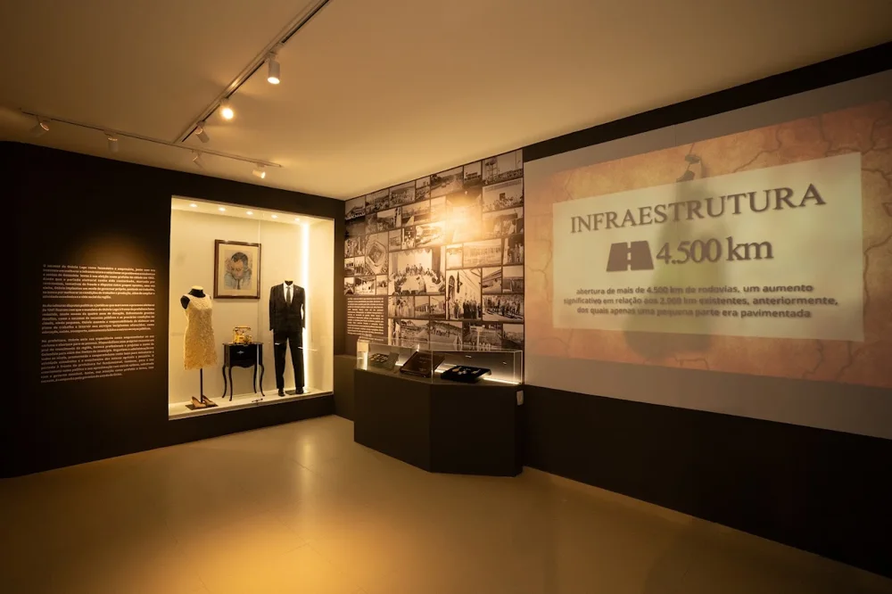 Sala da exposição Centenário de Otávio Lage, com vitrine de figurinos, mural de fotografias e projeção sobre infraestrutura